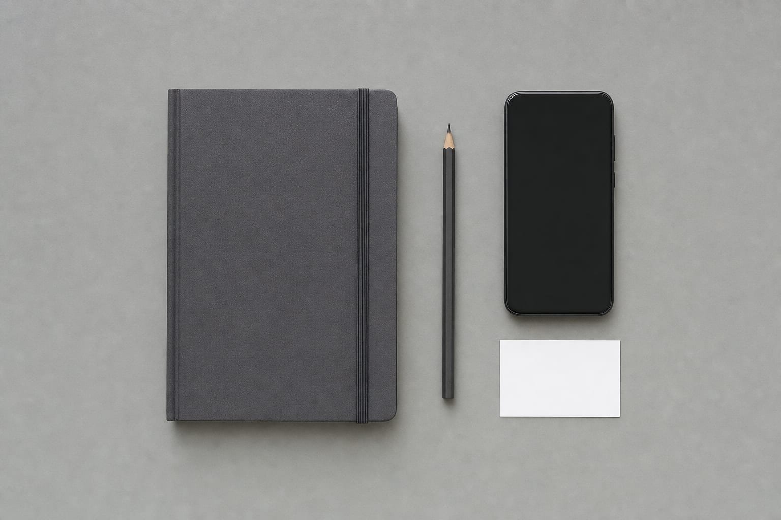 Minimal desk with a closed notebook, sharpened pencil, face-down smartphone, and a small blank card