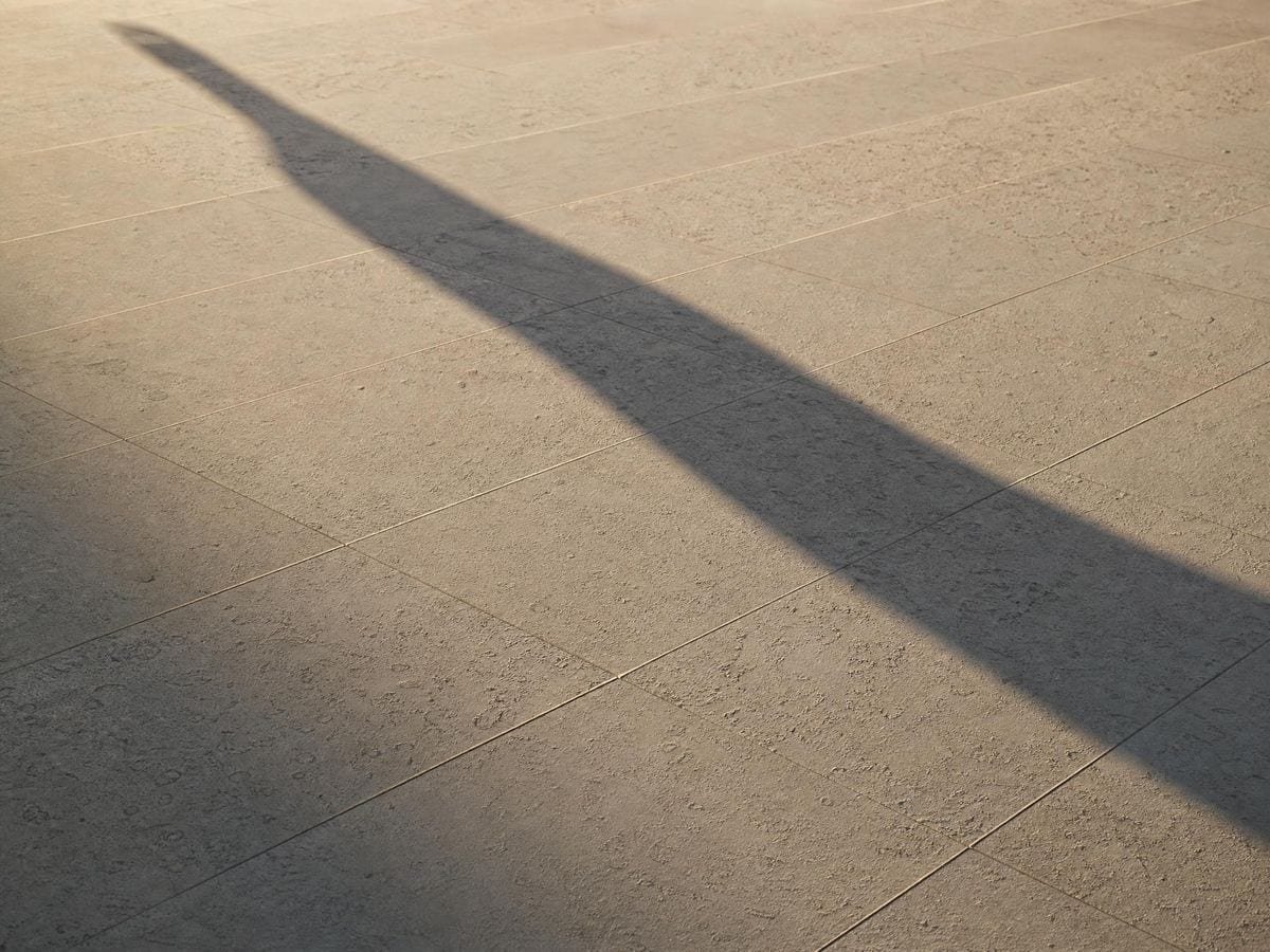 A long raking shadow stretched far across pale paving by a very low sun