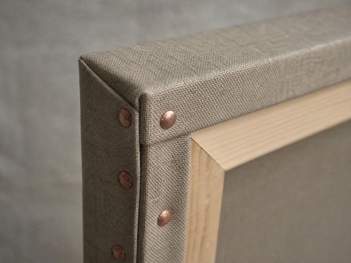 Raw linen pulled taut over a stretcher and folded at the corner with copper tacks