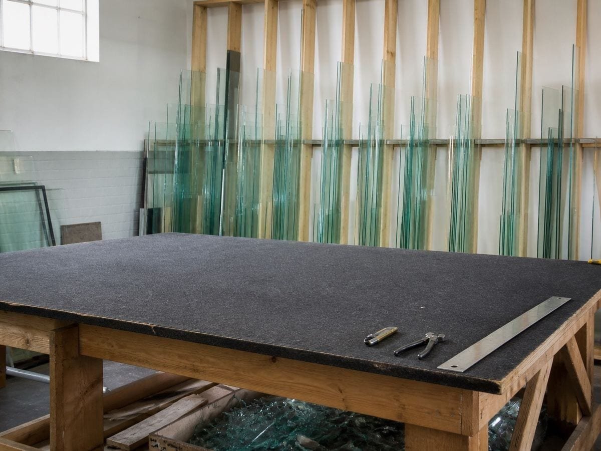 A glazier's cutting shop with a clear felt bench and picture glass racked by size behind