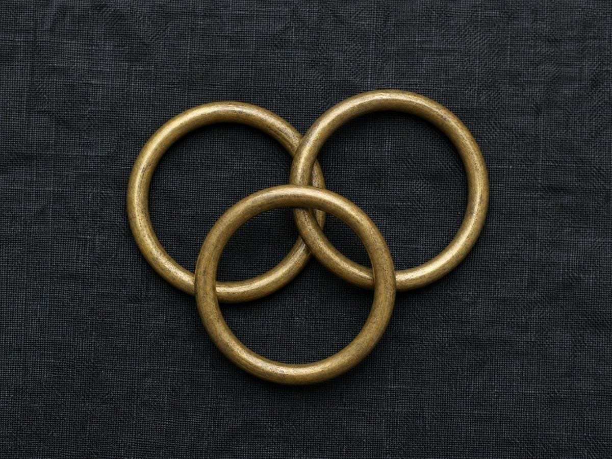 Three equal brass curtain rings lying loose and slightly overlapping on dark linen