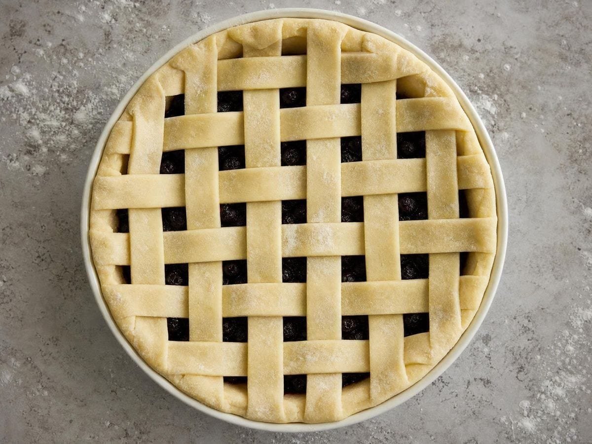 A woven lattice pastry lid on an unbaked pie, strips crossing in two directions
