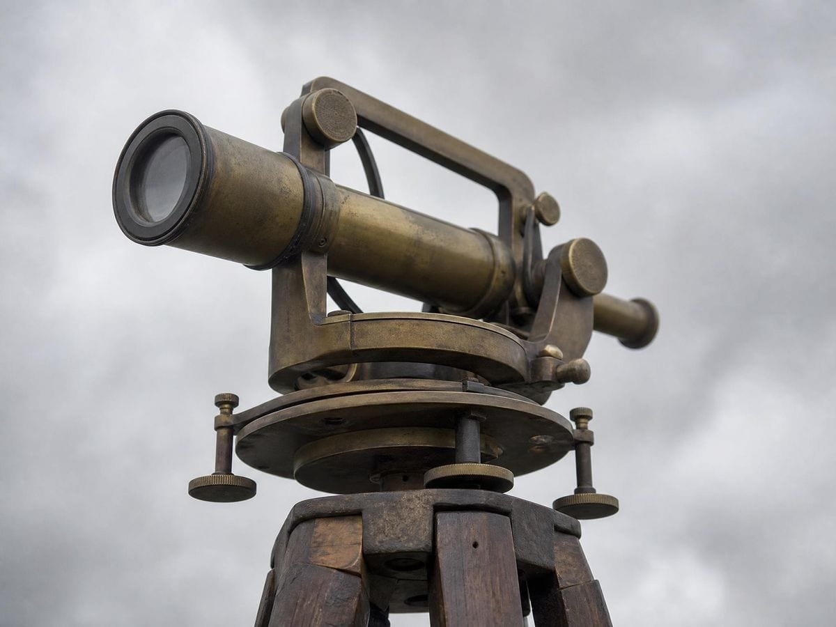 The brass head of an antique surveyor's theodolite mounted on a wooden tripod