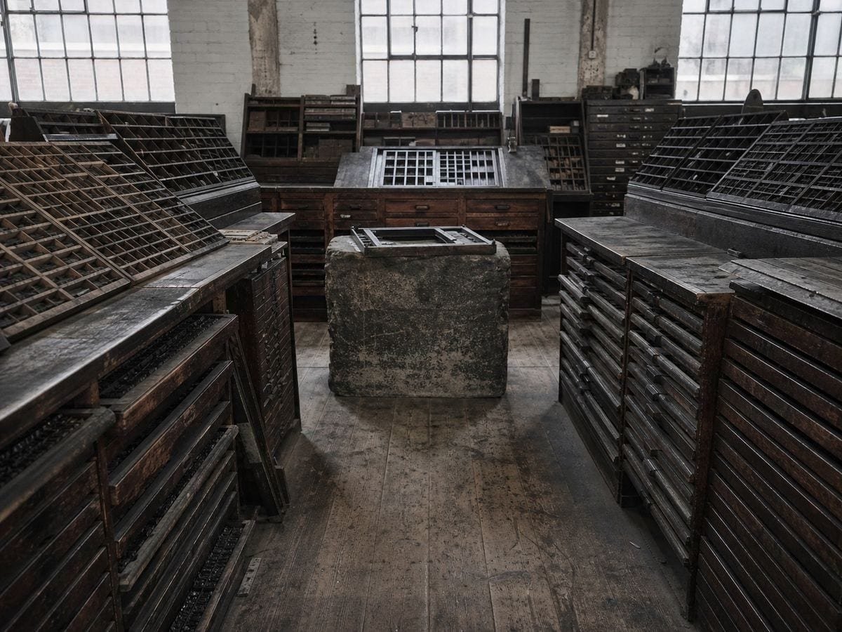 A letterpress composing room of sloped type frames with an empty chase on the stone