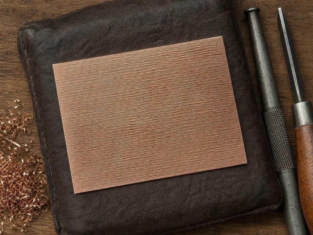 A copper engraving plate hatched in one direction with a lozenge burin beside it