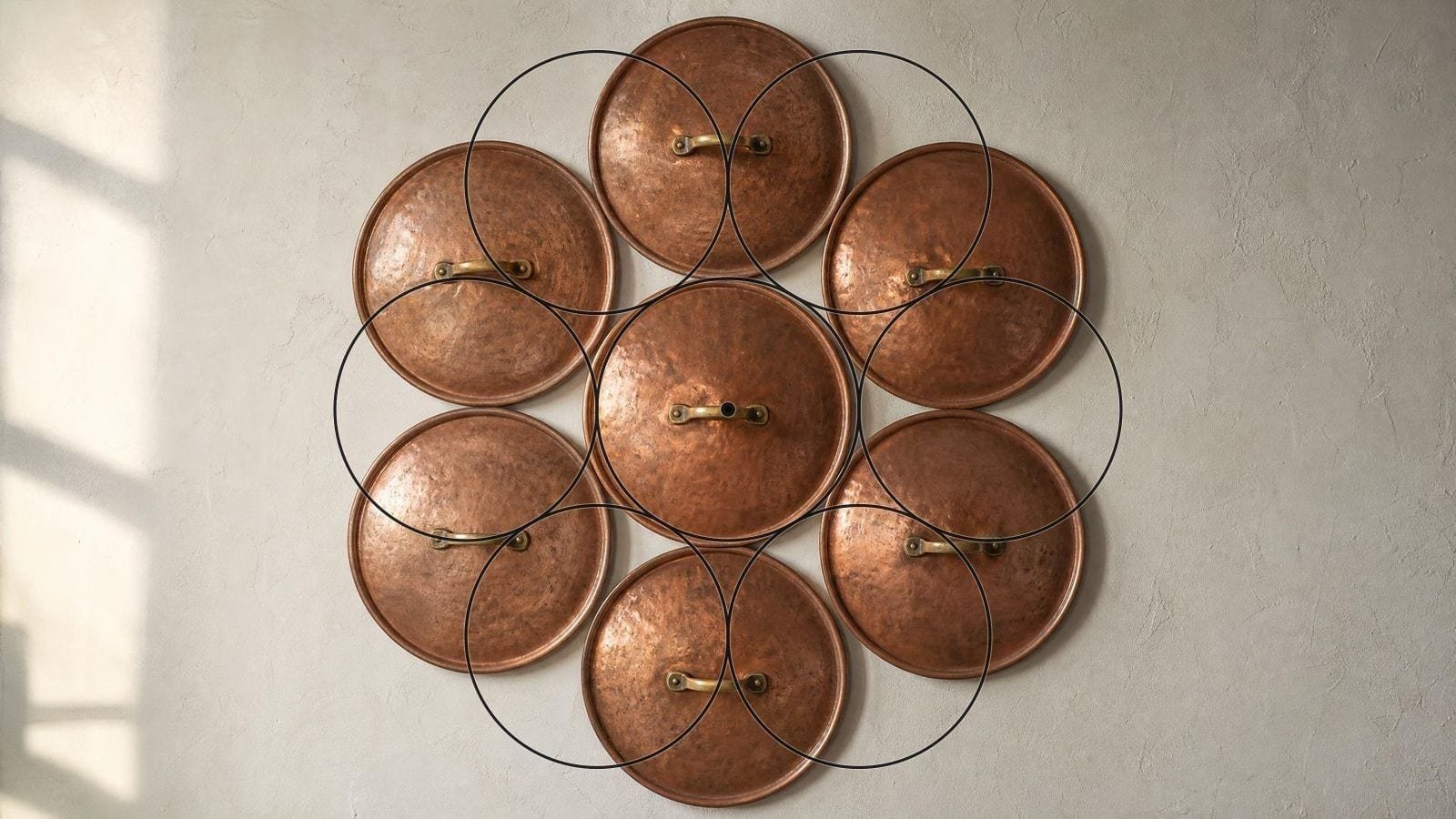Egg of Life overlay on seven copper pan lids arranged six around one on plaster