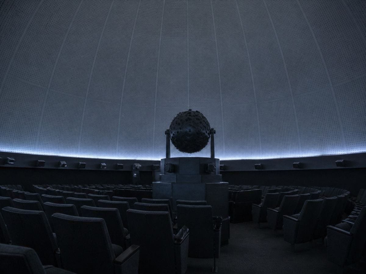 A planetarium chamber with the star projector at rest beneath a plain domed ceiling