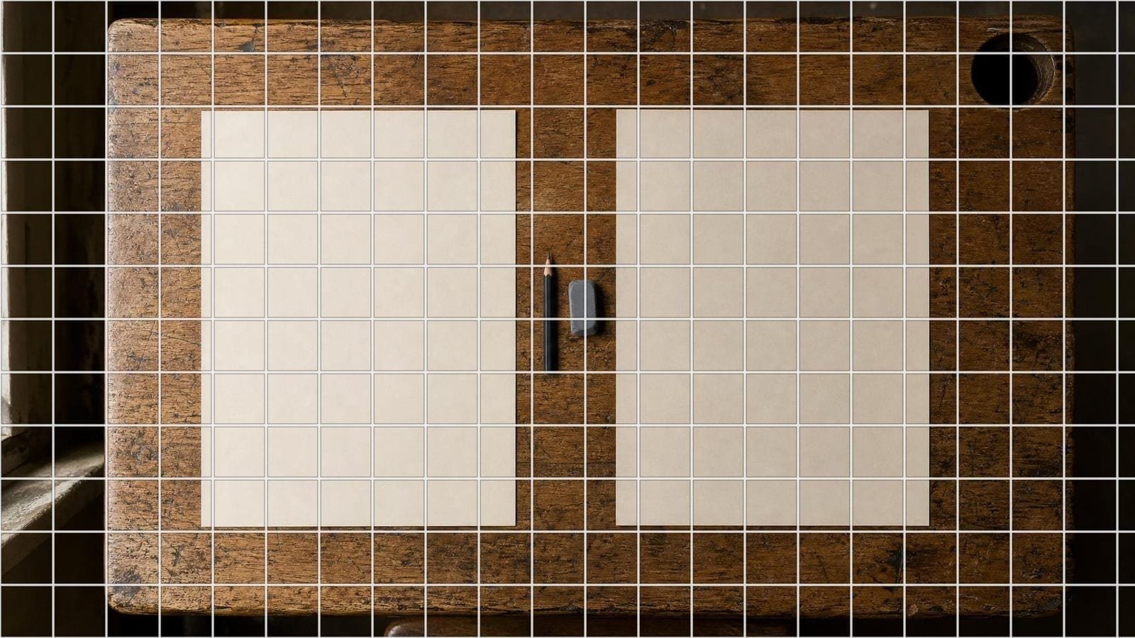 Grid drawing worksheet overlay on blank cartridge sheets and a pencil on a school desk