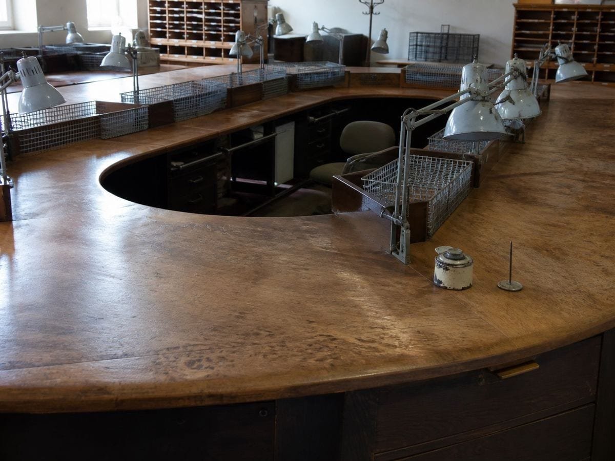A newspaper sub-editors' horseshoe desk cleared, with empty wire trays and unlit lamps
