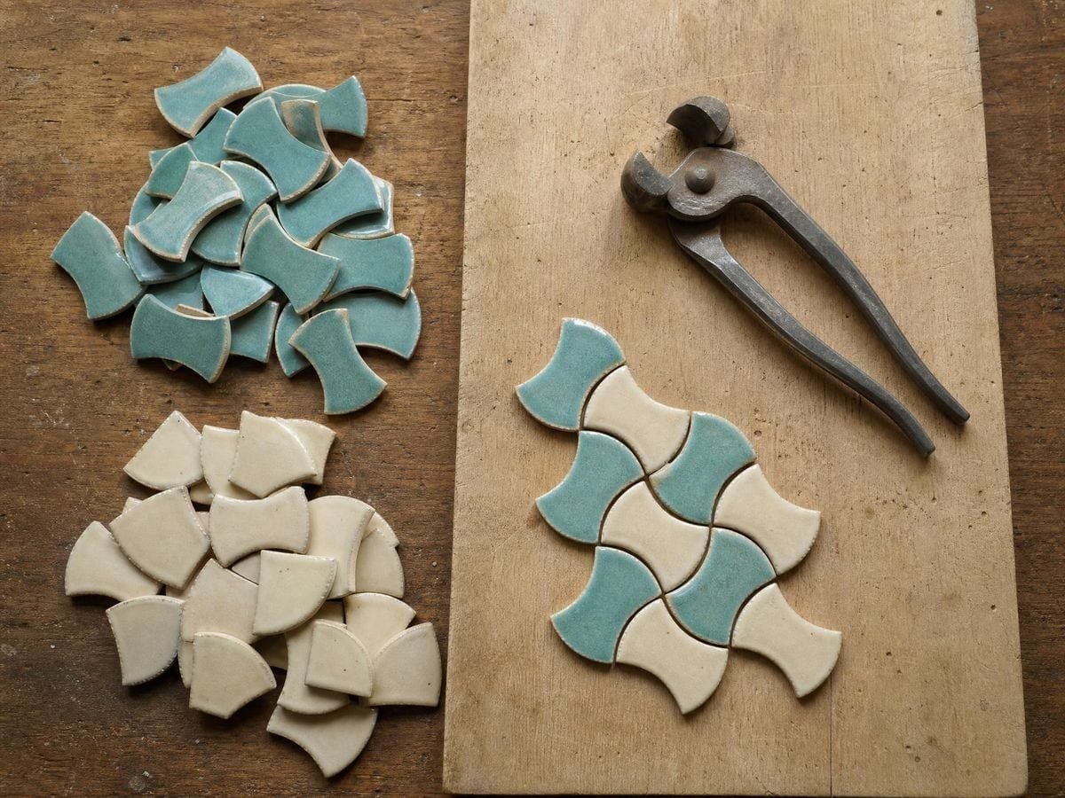 Hand-cut turquoise and cream glazed tile pieces sorted in heaps beside tile nippers