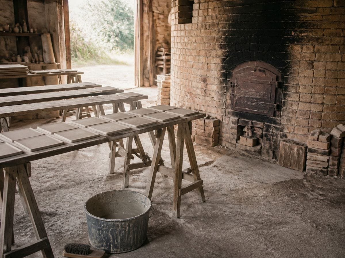 A tile workshop with a brick kiln and trestles of plain unglazed tiles drying