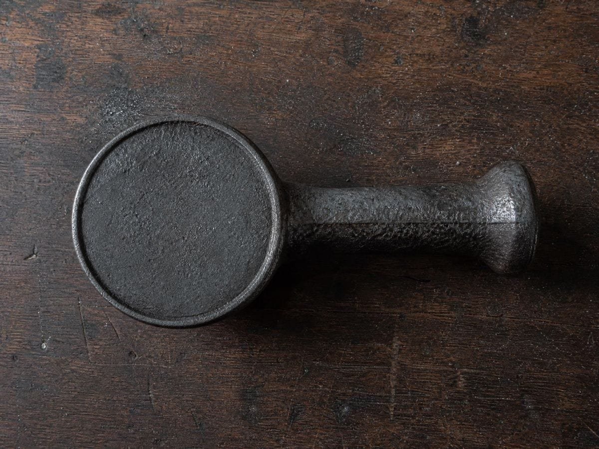 A cast iron branding stamp lying face up on a bench, its striking face unengraved