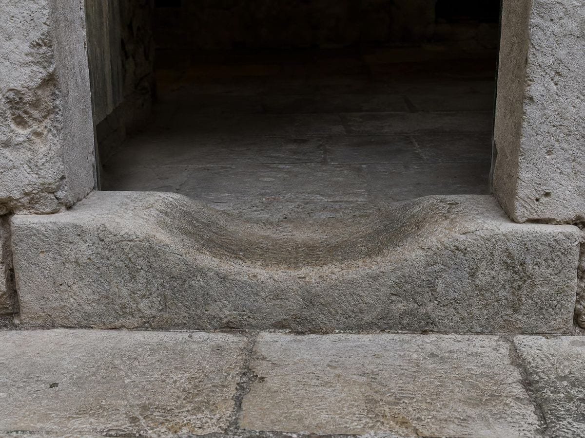 A limestone doorway threshold dished into a smooth hollow by generations of footfall