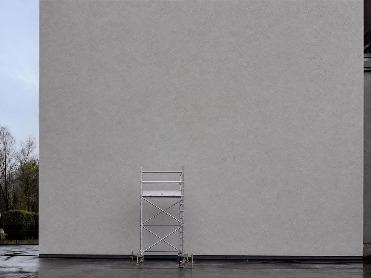 A mobile scaffold tower reaching barely a fifth of the way up an enormous blank wall