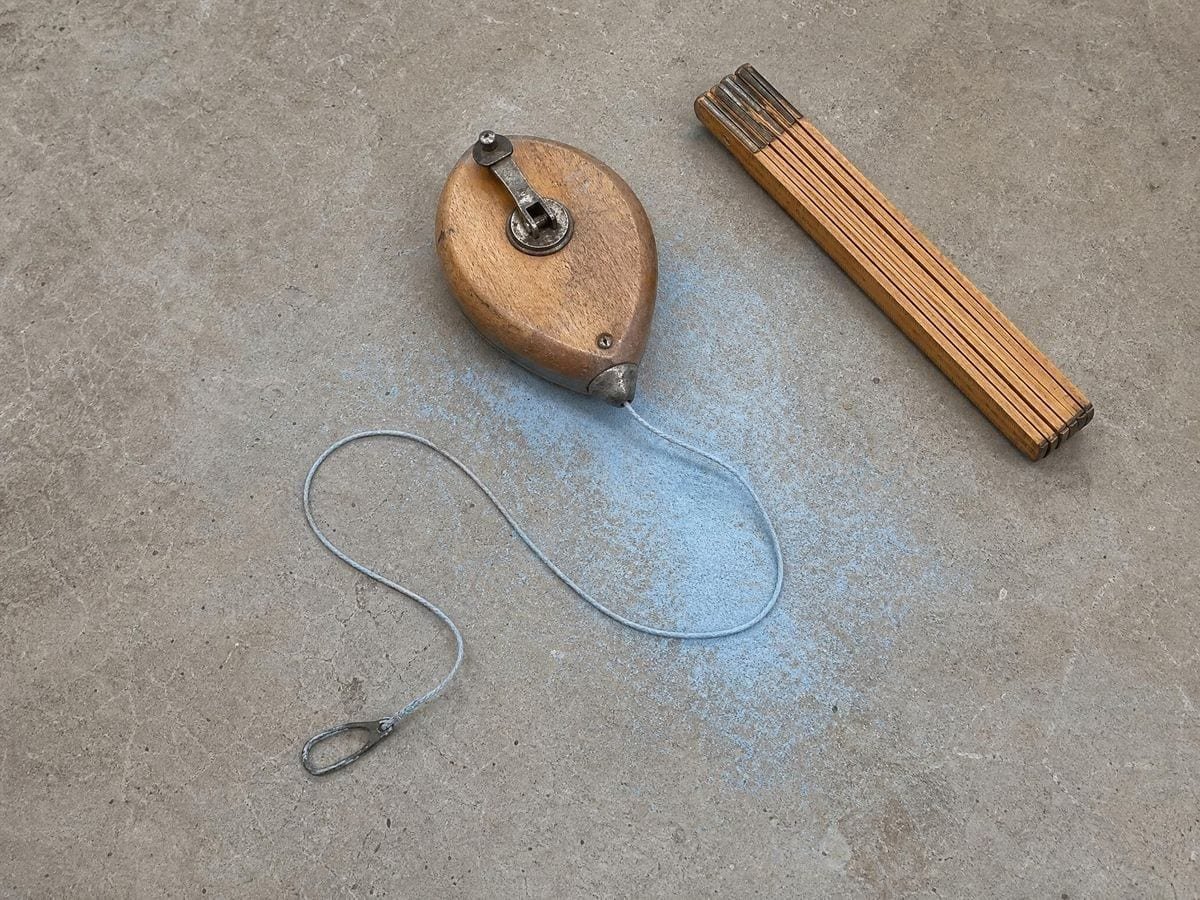 A decorator's chalk line reel on swept concrete with blue chalk dust scattered around it
