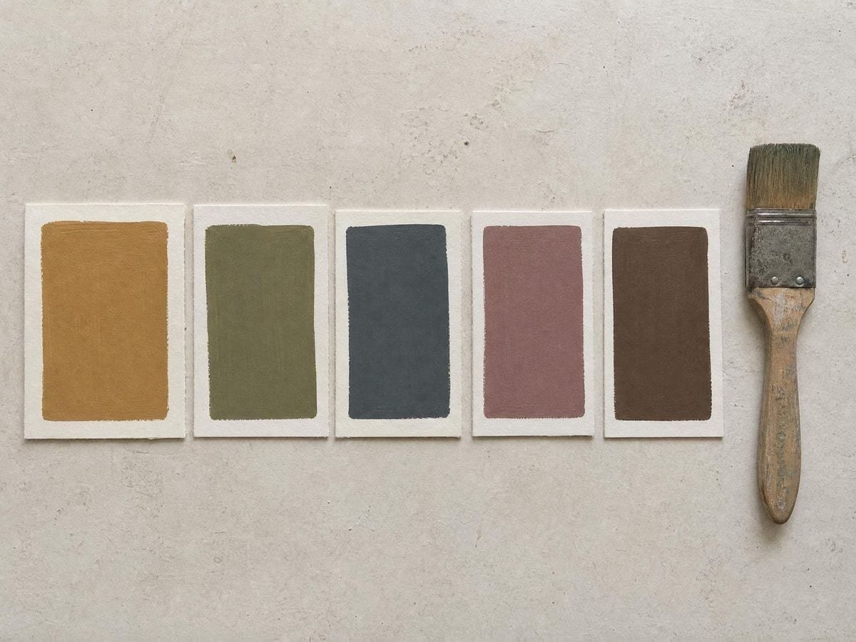 A row of flat hand-painted earth-tone swatches drying on off-white card