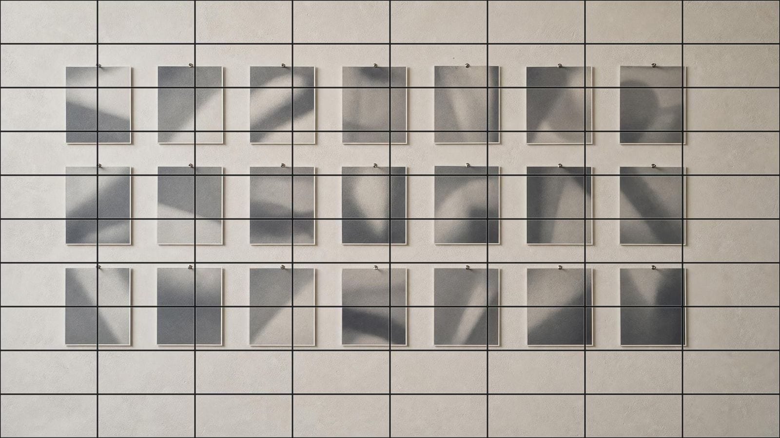 Photo grid overlay on an even array of small monochrome prints pinned to a studio wall