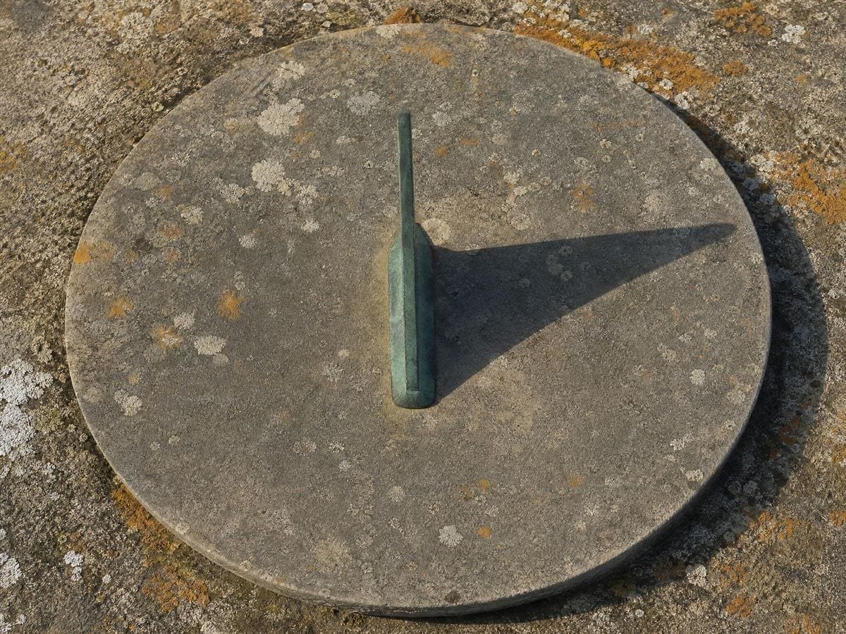 A weathered stone sundial with a bronze gnomon casting one clean shadow on plain stone