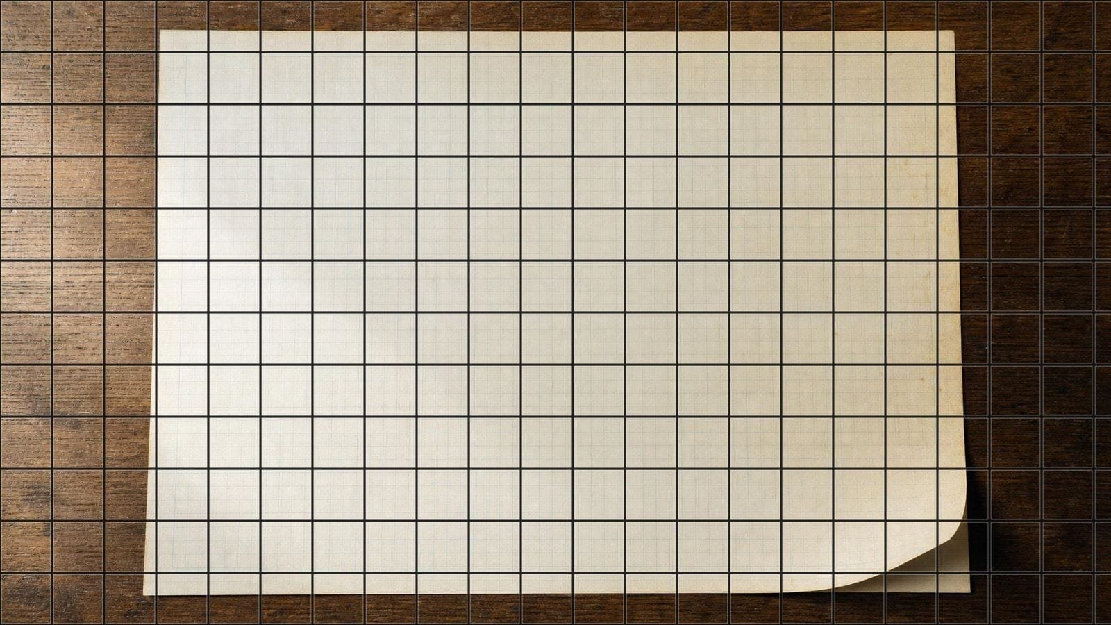 Printable graph paper overlay on a blank feint-ruled ledger sheet lying on an oak desk