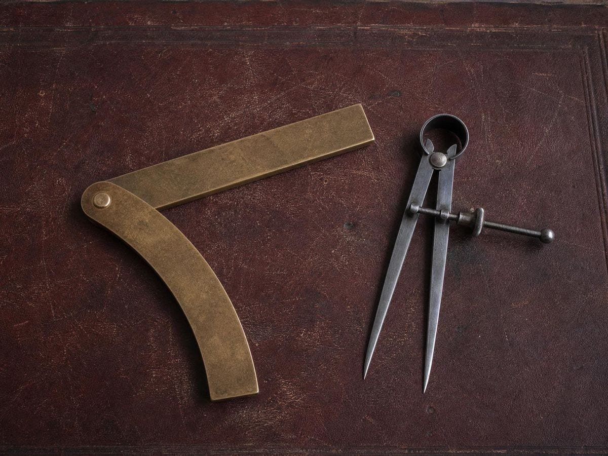 An antique hinged brass sector lying open beside a pair of steel spring dividers