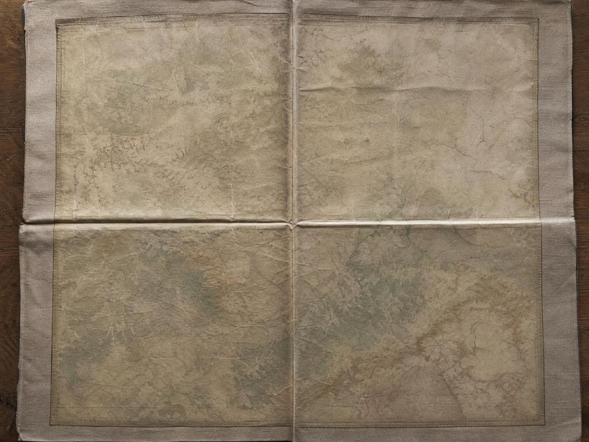 An old cloth-backed map opened flat, its fold creases crossing near the middle