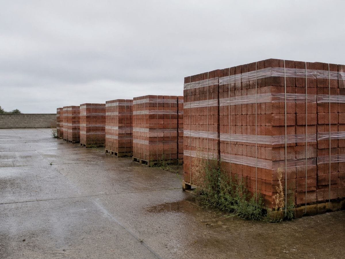 A brickyard of banded pallets of fired brick stacked in rows on damp concrete