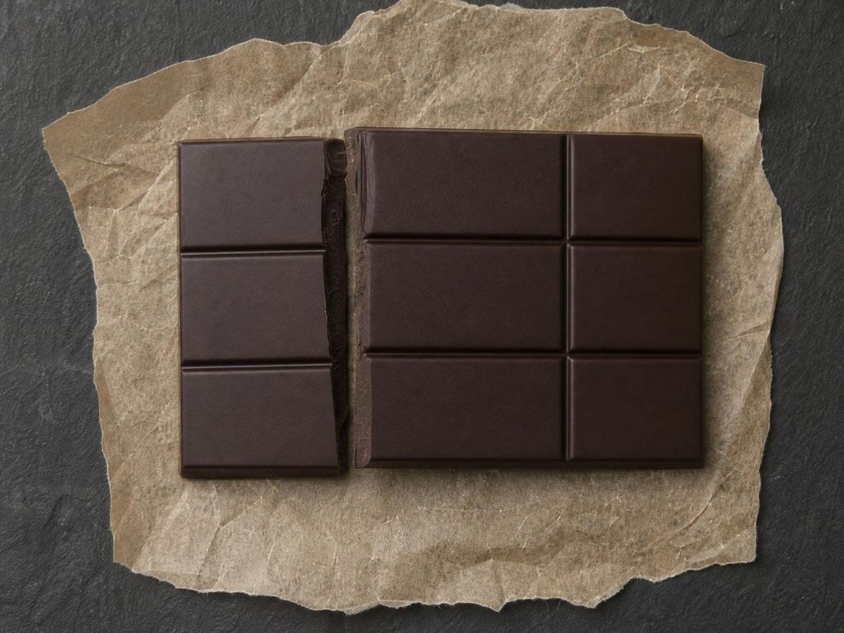 A bar of dark chocolate snapped along a moulded line, sections wider than deep