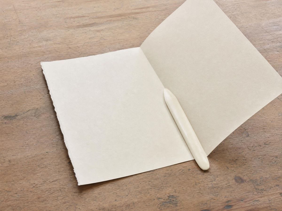 A bone folder lying along a fresh crease in a large sheet of cream laid paper