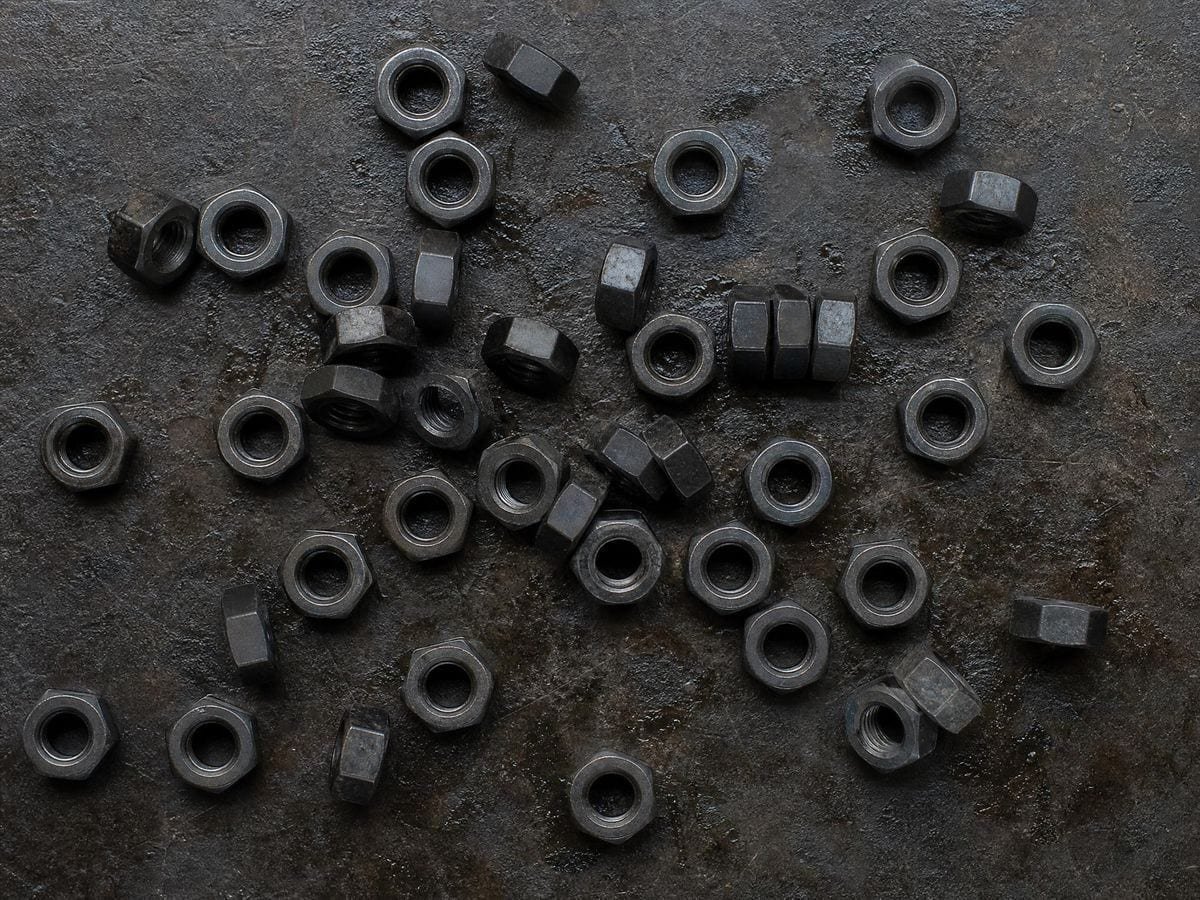 Steel hexagonal nuts of one size scattered loose on a scarred steel workbench