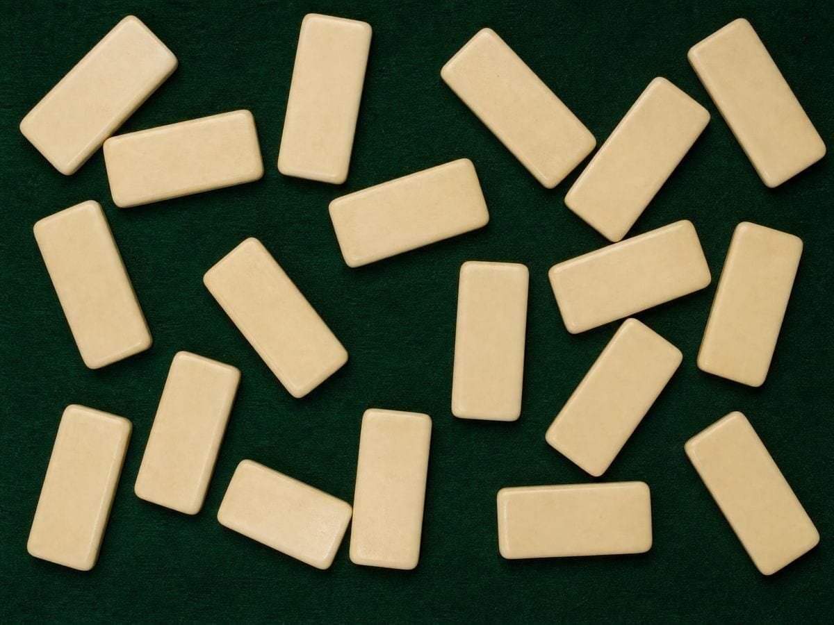 Plain bone-coloured domino tiles face down on green baize, each twice as long as wide