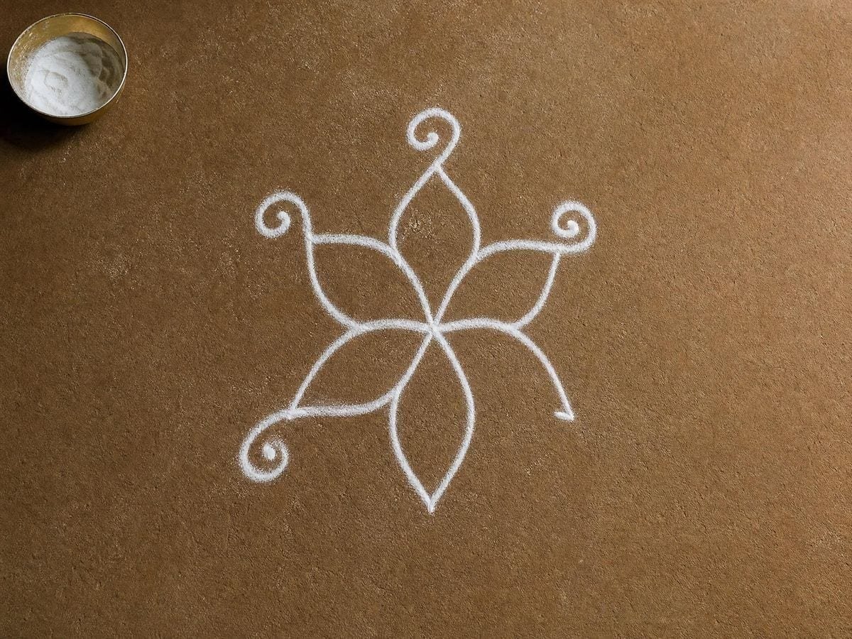 A symmetrical rice-flour figure part drawn on a swept earth threshold beside a brass bowl