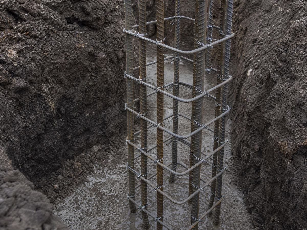 A tied steel reinforcement cage standing in a trench, bars at even spacing