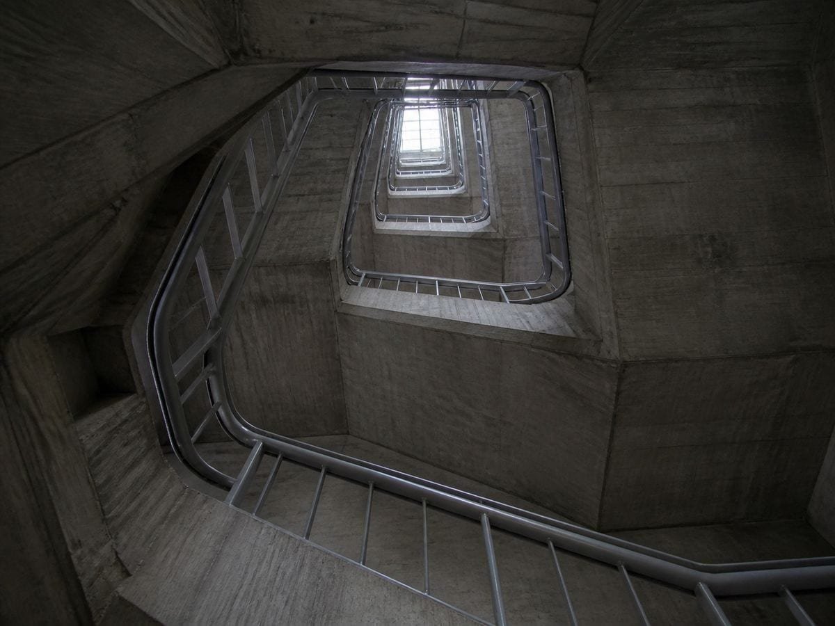 A concrete stairwell void seen straight up, flights narrowing toward a small rooflight