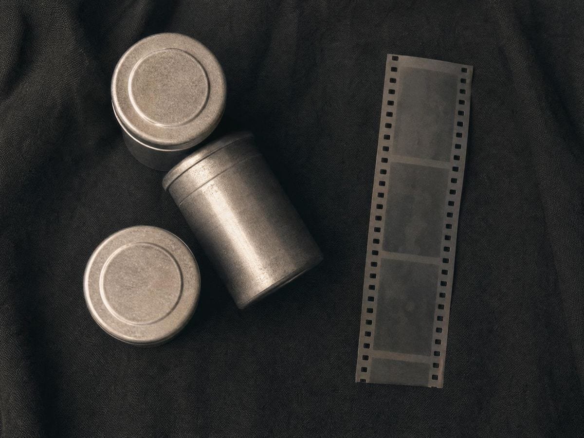 Three metal film canisters beside a loose strip of developed negative with sprocket holes