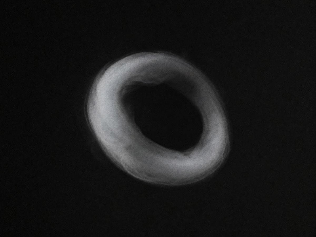 A single pale smoke ring holding its form in still air with its centre open