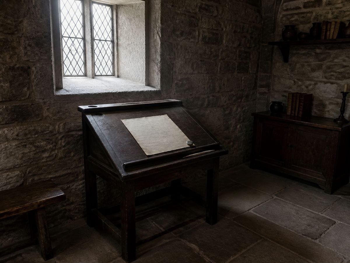 A monastic scriptorium writing slope beneath a deep-set window with an inkhorn and quill